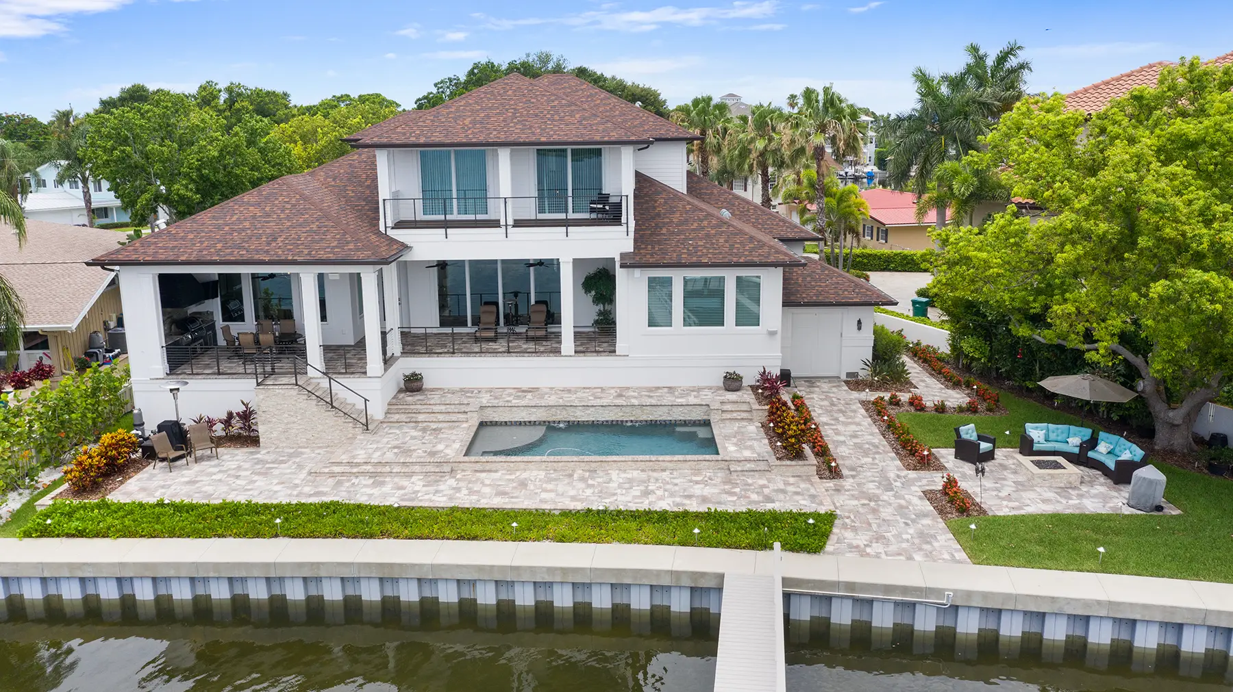 Waterfront luxury home with a modern design, spacious patio, swimming pool, and landscaped outdoor seating area, built by Gulf Wind Homes.